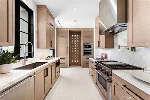 kitchen with backsplash, light stone counters, stainless steel appliances, wall chimney exhaust hood, and a sink