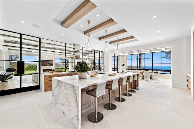 kitchen with a wealth of natural light, beam ceiling, a large island with sink, and light stone countertops