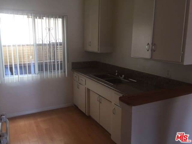 kitchen with white cabinets, sink, light wood-type flooring, and kitchen peninsula