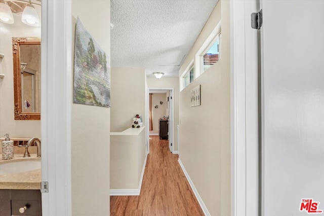 corridor featuring sink, light hardwood / wood-style flooring, and a textured ceiling