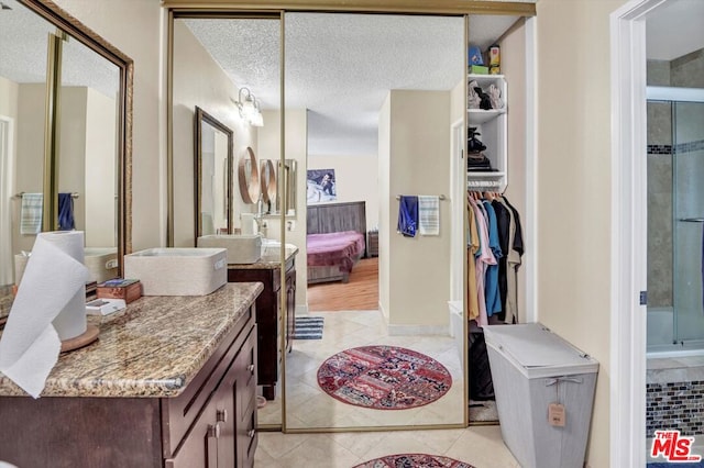 bathroom featuring vanity, a shower with shower door, tile patterned flooring, and a textured ceiling