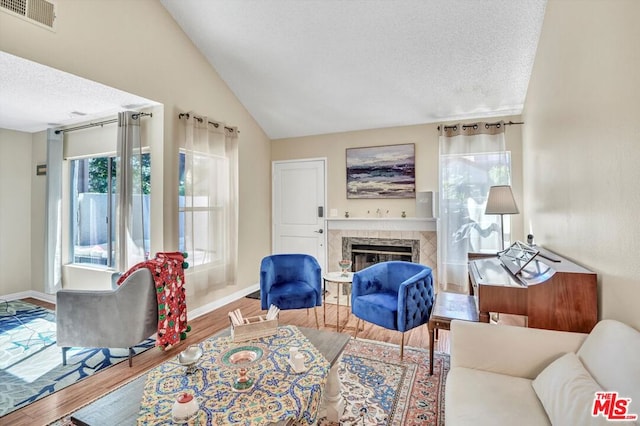 living room featuring hardwood / wood-style floors, a fireplace, a textured ceiling, and vaulted ceiling