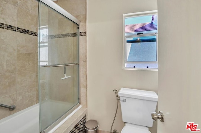 bathroom featuring combined bath / shower with glass door, a wealth of natural light, and toilet