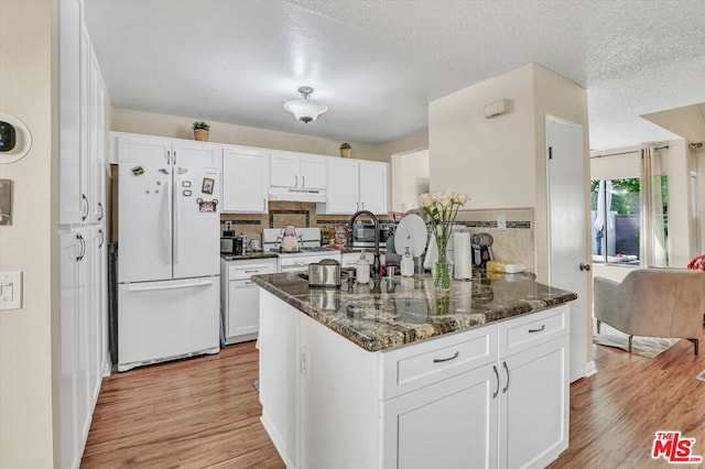 kitchen featuring white appliances, dark stone countertops, light hardwood / wood-style flooring, and white cabinets