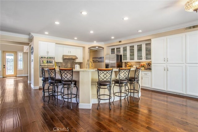 kitchen with a kitchen island with sink, white cabinets, decorative backsplash, appliances with stainless steel finishes, and dark hardwood / wood-style flooring