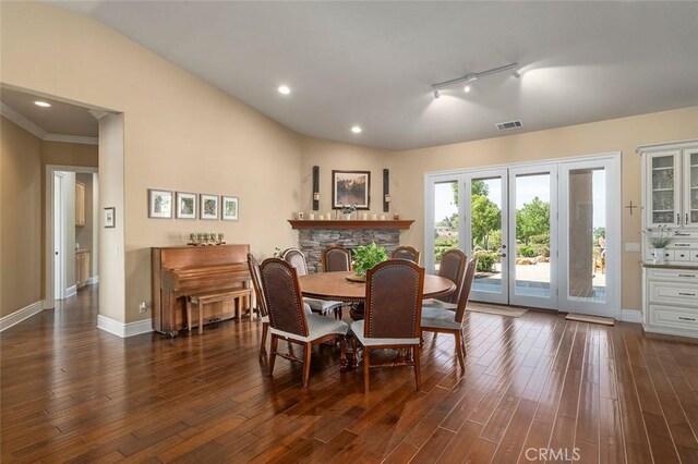 dining area featuring a stone fireplace, crown molding, track lighting, and dark hardwood / wood-style floors