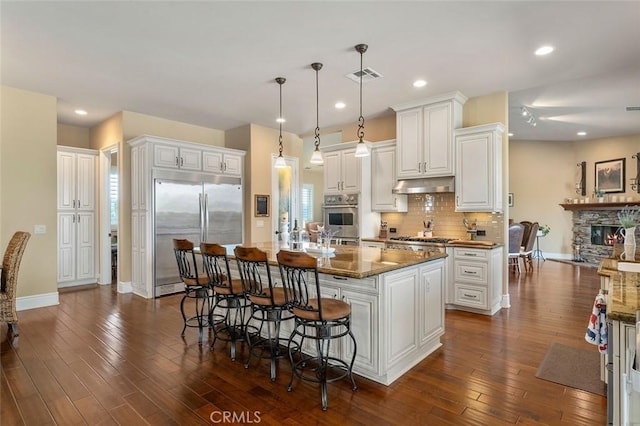 kitchen featuring a kitchen island with sink, hanging light fixtures, dark hardwood / wood-style floors, appliances with stainless steel finishes, and white cabinetry