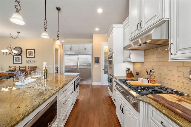 kitchen with white cabinets, hanging light fixtures, dark hardwood / wood-style floors, appliances with stainless steel finishes, and a notable chandelier