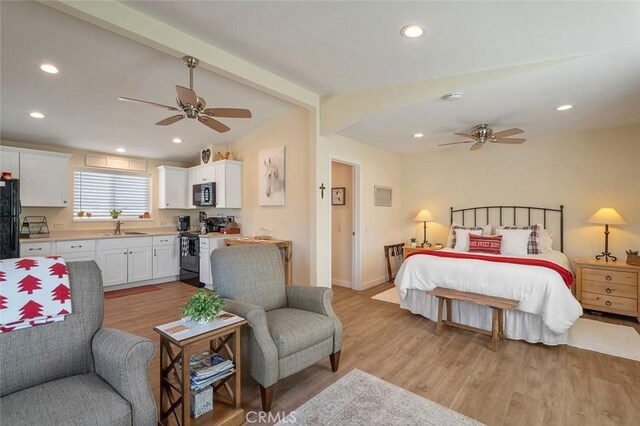 bedroom featuring ceiling fan, sink, vaulted ceiling with beams, black refrigerator, and light wood-type flooring