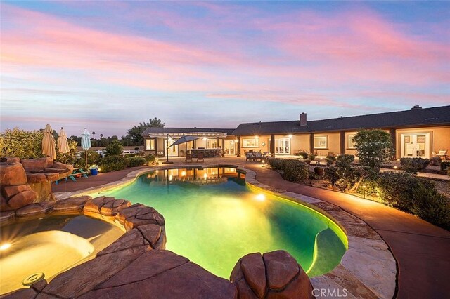 pool at dusk featuring a jacuzzi and a patio