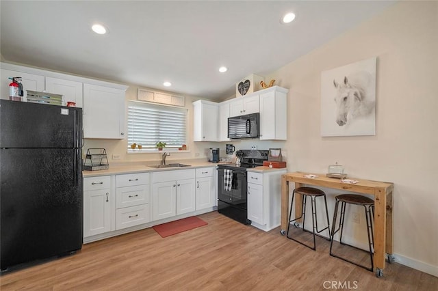 kitchen featuring black appliances, white cabinets, sink, vaulted ceiling, and light hardwood / wood-style floors