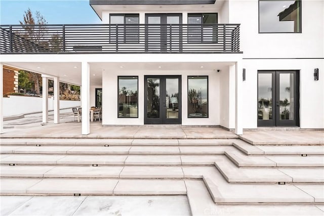 view of exterior entry with french doors, a balcony, and a patio area