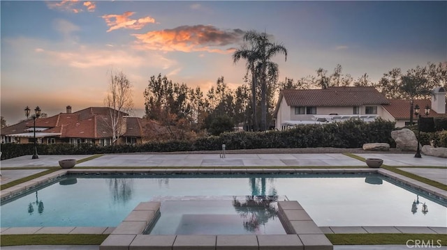 pool at dusk with an in ground hot tub