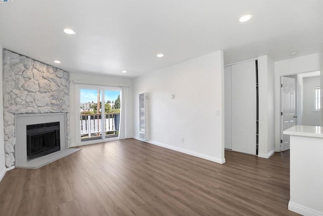 unfurnished living room featuring a stone fireplace and dark wood-type flooring