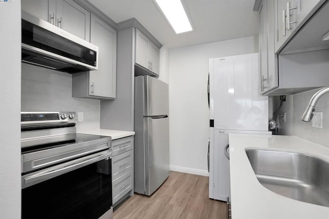 kitchen with backsplash, stainless steel appliances, gray cabinetry, and light hardwood / wood-style floors