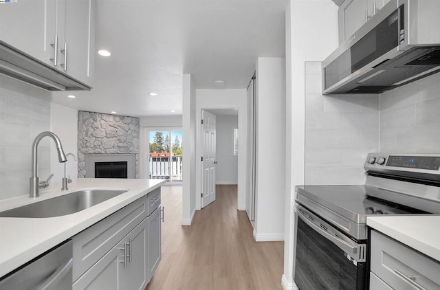 kitchen featuring appliances with stainless steel finishes, light hardwood / wood-style floors, sink, gray cabinets, and a stone fireplace