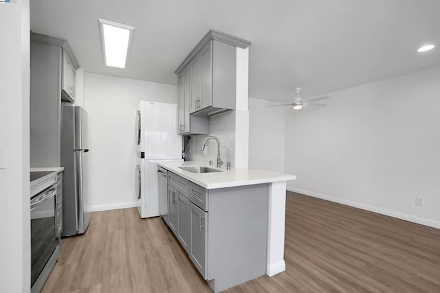 kitchen with appliances with stainless steel finishes, light wood-type flooring, gray cabinets, and sink