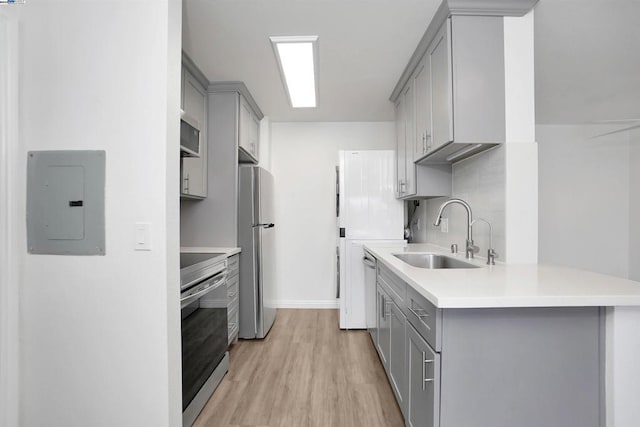 kitchen featuring gray cabinetry, sink, backsplash, light hardwood / wood-style floors, and appliances with stainless steel finishes