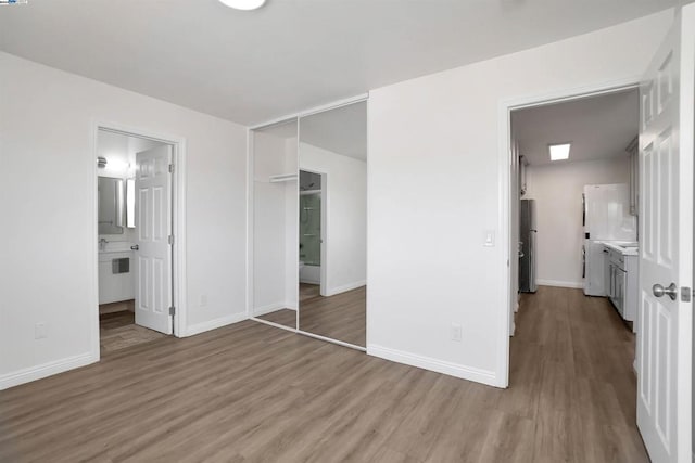 unfurnished bedroom with a closet, light hardwood / wood-style floors, stainless steel refrigerator, and ensuite bath