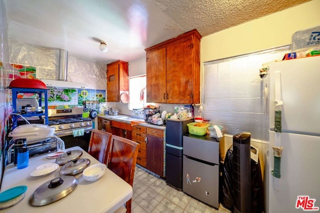 kitchen featuring stainless steel gas range oven, white refrigerator, sink, and light tile patterned floors