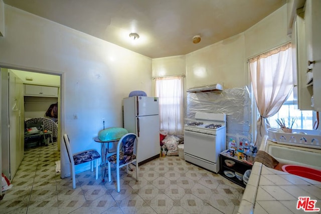 kitchen featuring wall chimney range hood, plenty of natural light, white appliances, and tile countertops