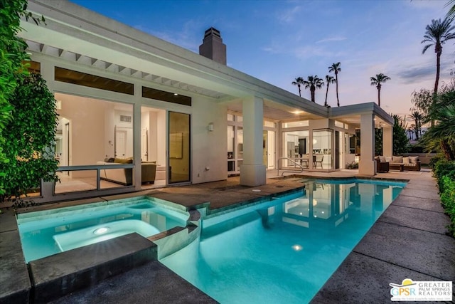 pool at dusk featuring an in ground hot tub, an outdoor hangout area, and a patio area