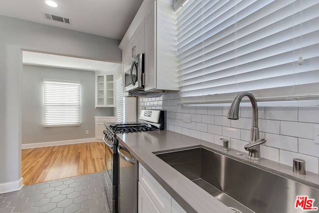 kitchen with stainless steel appliances, white cabinets, sink, light tile patterned floors, and backsplash