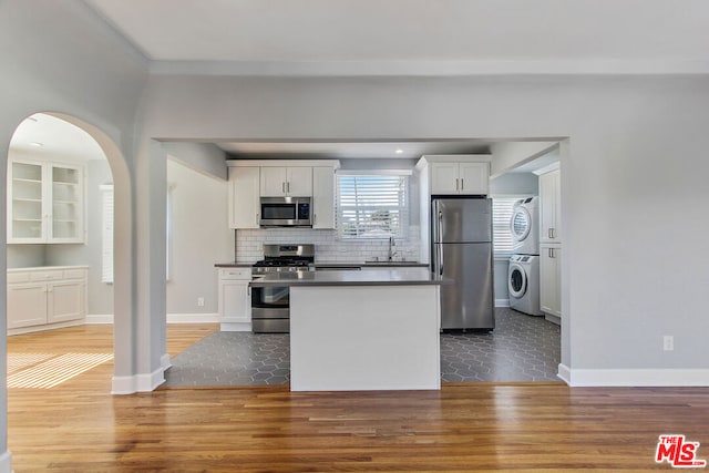 kitchen featuring tile patterned floors, stainless steel appliances, white cabinets, stacked washer and dryer, and backsplash