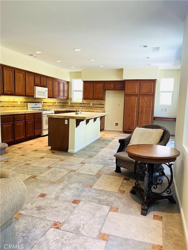 kitchen featuring backsplash, a center island, a breakfast bar, and white appliances