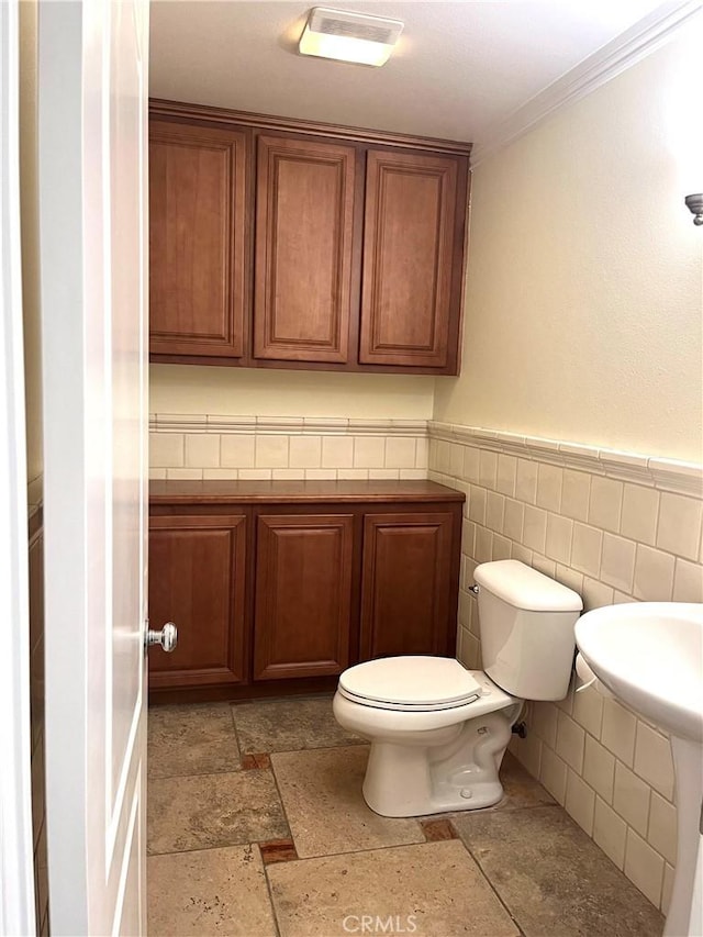 bathroom with toilet, crown molding, and tile walls