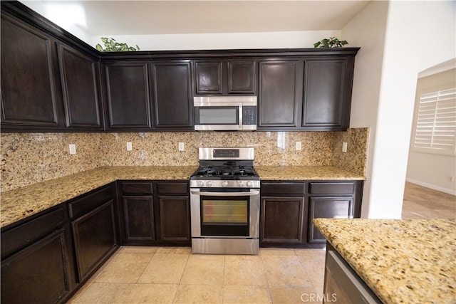 kitchen featuring appliances with stainless steel finishes, light tile patterned flooring, decorative backsplash, and light stone counters