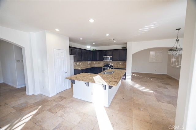 kitchen with light tile patterned flooring, backsplash, light stone countertops, appliances with stainless steel finishes, and a kitchen breakfast bar