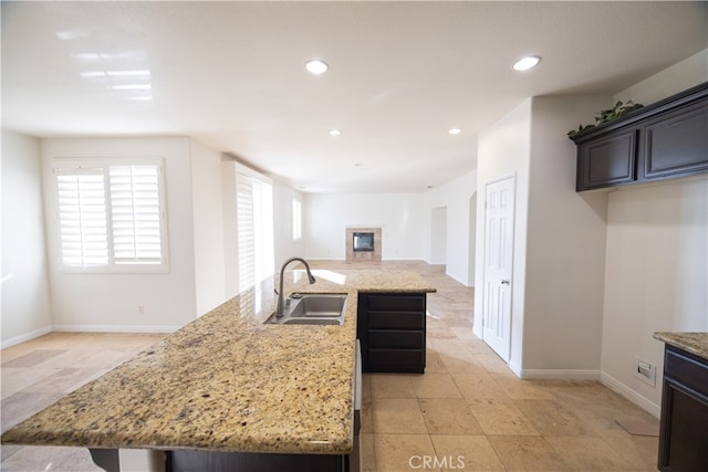 kitchen with light tile patterned flooring, a kitchen island, sink, and light stone counters