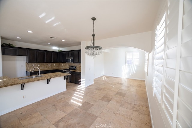 kitchen featuring appliances with stainless steel finishes, a breakfast bar area, light stone counters, backsplash, and light tile patterned flooring