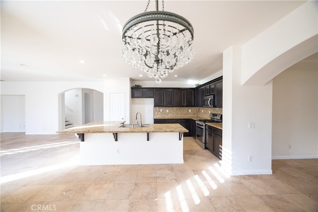 kitchen with tasteful backsplash, light stone countertops, appliances with stainless steel finishes, light tile patterned floors, and a kitchen island with sink