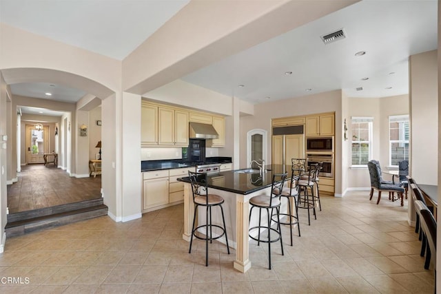 kitchen with a kitchen island with sink, exhaust hood, sink, built in appliances, and light tile patterned flooring