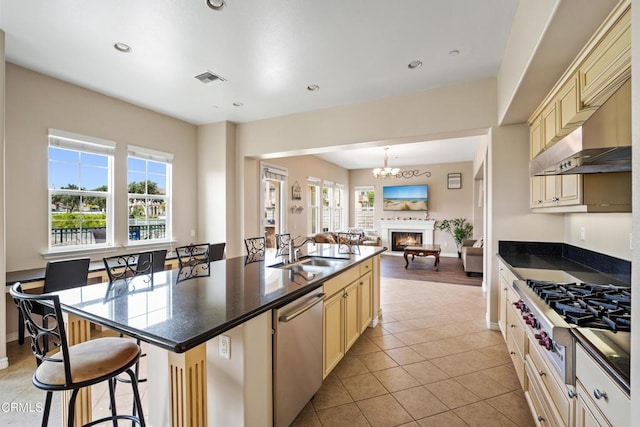 kitchen with sink, a kitchen breakfast bar, cream cabinetry, a kitchen island with sink, and appliances with stainless steel finishes