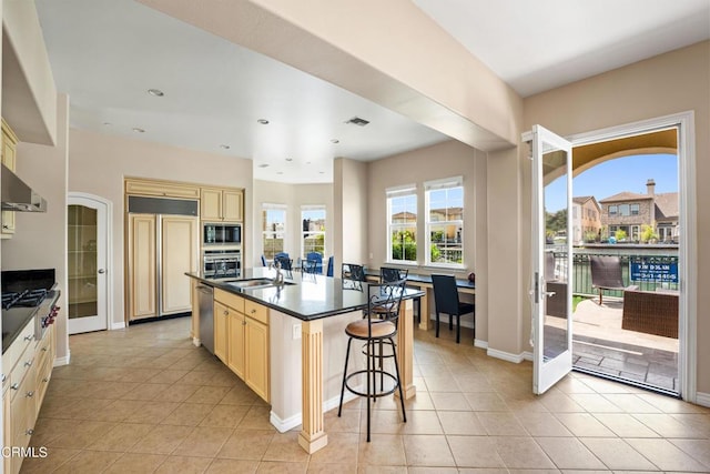 kitchen with a breakfast bar, a kitchen island with sink, sink, light tile patterned floors, and built in appliances