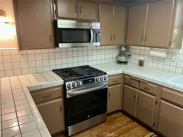 kitchen with light hardwood / wood-style floors, appliances with stainless steel finishes, tile countertops, and backsplash