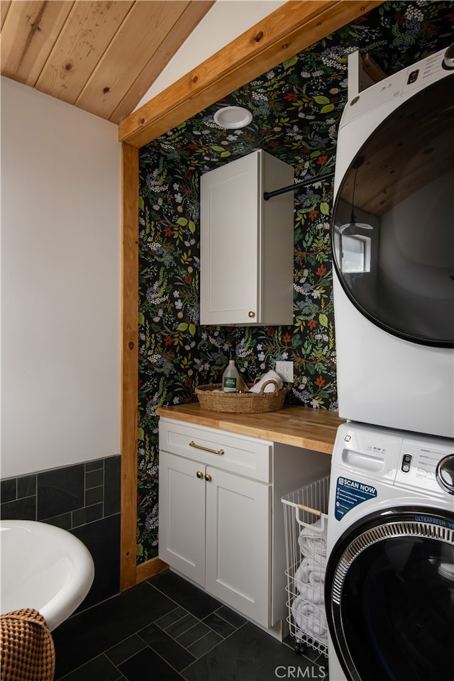 washroom featuring stacked washer and clothes dryer, dark tile patterned flooring, and wood ceiling