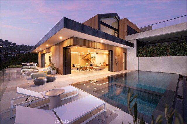 pool at dusk with outdoor lounge area and a patio area