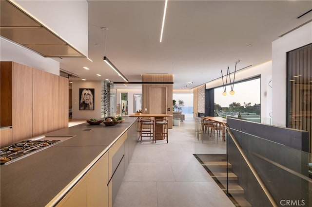 kitchen with stainless steel gas stovetop, light brown cabinetry, pendant lighting, and a breakfast bar