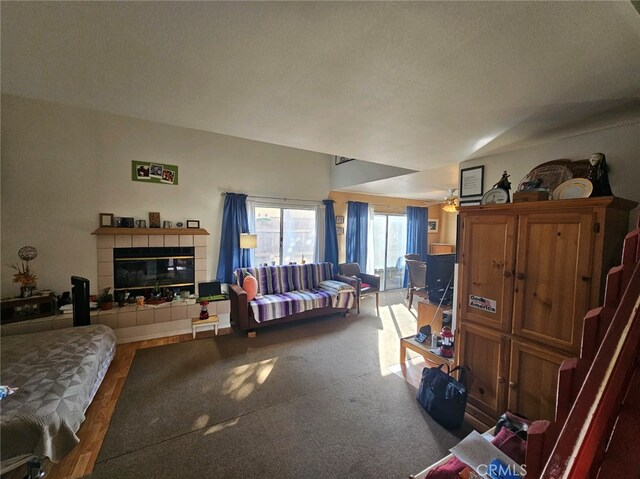 living room featuring a tile fireplace, ceiling fan, carpet floors, and a textured ceiling