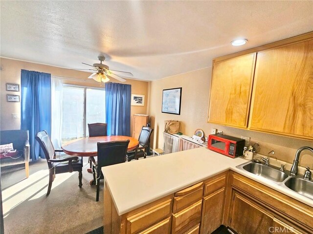 kitchen with ceiling fan, sink, kitchen peninsula, carpet floors, and a textured ceiling