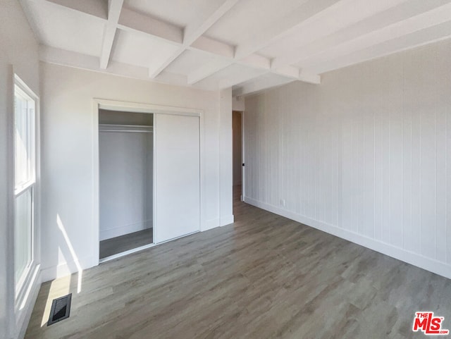 unfurnished bedroom featuring coffered ceiling, beam ceiling, wood-type flooring, and a closet