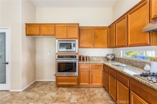 kitchen featuring light stone counters, brown cabinets, stainless steel appliances, and under cabinet range hood