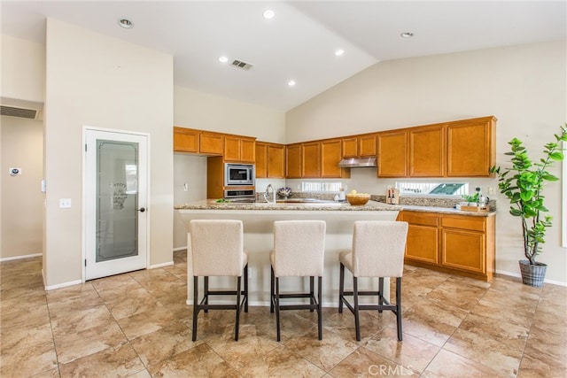 kitchen with a center island with sink, visible vents, under cabinet range hood, stainless steel microwave, and brown cabinets