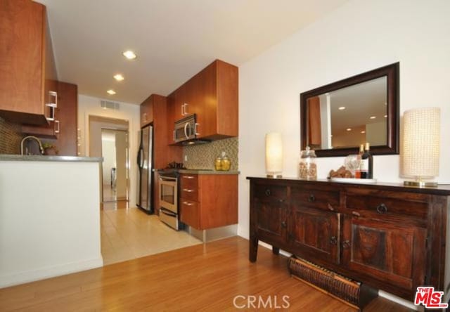 kitchen with sink, decorative backsplash, appliances with stainless steel finishes, and light wood-type flooring