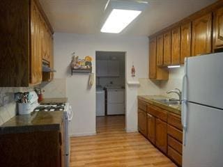 kitchen featuring white refrigerator, light wood-type flooring, sink, washer and dryer, and stove