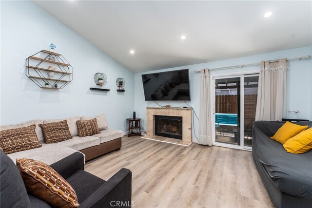 living room featuring light wood-type flooring, lofted ceiling, and a tile fireplace